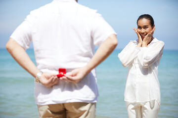 close up young man hands hiding engagement ring for surprise his girlfriend on the beach