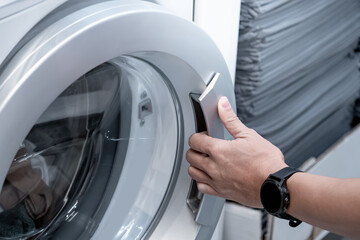 Male hand opening automatic washing machine door in laundry room.