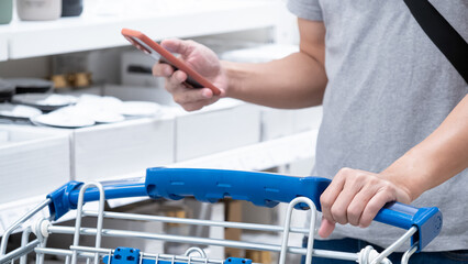 Customer hand using smartphone white holding shopping cart in grocery store or supermarket.