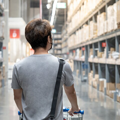 Male customer holding shopping cart looking for goods in grocery store or supermarket aisle.