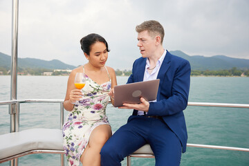 businessman using laptop computer and talking with his partner on luxury yacht