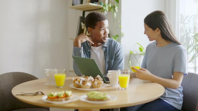 Multiethnic couple about to shopping online during breakfast at home