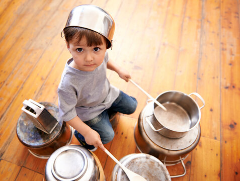 Portrait, boy child playing drums on pots on a floor, curious and enjoying music. Face, top view and kid with pans for musical entertainment, silly and carefree in kitchen in his home on the weekend