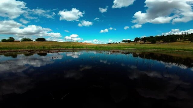 reflection of clouds in the lake. Drone FPV Ariel shot of pond and tall grass. drone flying over fields