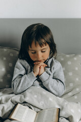 Little girl pray and read in bed with an Bible next to her - 602395605