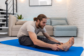 Man practicing yoga at home on floor on yoga mat stretching body.