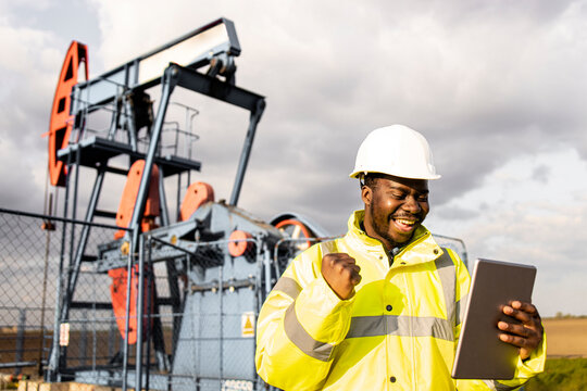 Production of crude oil. Oil field worker holding tablet computer and celebrating success.