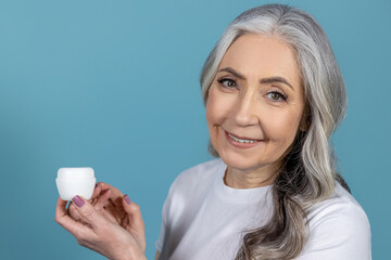 Long-haired senior good-looking woman holding a jar of face cream