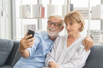 Happy husband and wife senior couple elderly family, caucasians mature, adult lover and retired man, woman using smartphone selfie on cozy sofa, couch at home together. Comfortable, relax people.