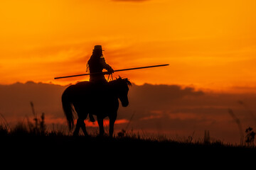 silhouette of a rider with a horse with a long spear against the setting sun