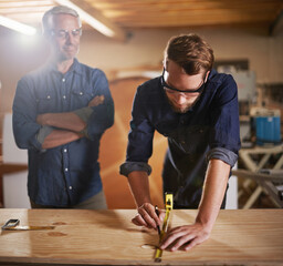 Mentor carpenter, apprentice and wood measurement at designer furniture manufacturing workshop....