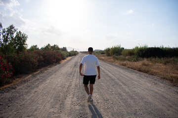 Boy walking on a dirt path in a field. Man walking along a path. Moroccan boy taking a stroll. Man walking in a field wearing a white t-shirt. Boy walking calmly through the countryside.
