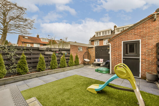 a backyard area with a green lawn and yellow plastic toy on the ground in front of a brick wall behind it