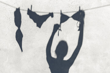 summer, laundry and silhouette concept - shadow of woman hanging lingerie or swimwear on rope...