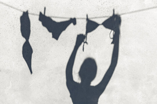 summer, laundry and silhouette concept - shadow of woman hanging lingerie or swimwear on rope outdoors
