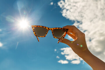 food, dessert and eating concept - close up of hand holding sunglasses over blue sky and cloud