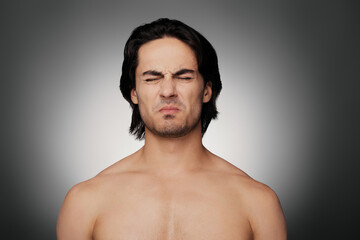 Fototapeta premium Portrait of displeased young shirtless man keeping eyes closed against grey background