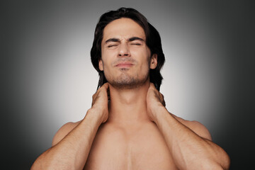 Fototapeta premium Portrait of displeased shirtless man suffering from neck ache against grey background