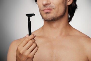 Close-up of displeased young man holding razor while shaving against grey background