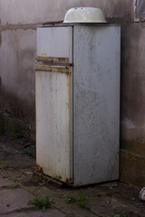 An old rusty refrigerator was thrown away on the street in sun light concrete wall on background Close-up