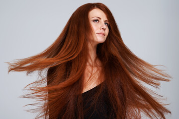 Red hair, wind and face of woman in studio for treatment, wellness and movement on gray background. Beauty, hairdresser salon and female model with keratin shine, healthy and natural hairstyle