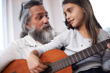 Grandfather teaching girl to play guitar, learning and development in music with help in...