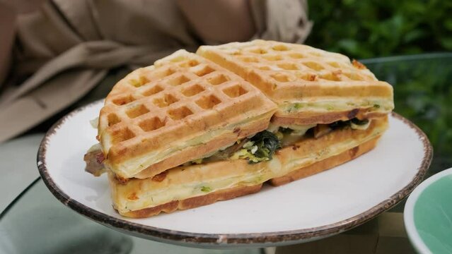 Waffle sandwich with spinach, mushrooms and cheese in a plate outdoor in sidewalk cafe. Close up