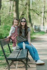 A female toddler in velvet overall is on the bench with her mother.