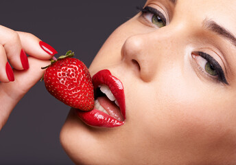Beauty, portrait and model with a strawberry in studio with red nails and lipstick cosmetics. Health, wellness and closeup of woman with makeup eating fruit for nutrition isolated by gray background.