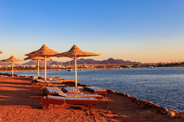 Sun umbrellas and chaise lounges on tropical beach. Concept of rest, relaxation, holidays, resort