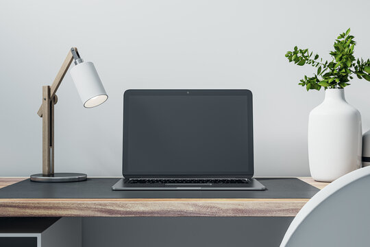 Closeup front view of a home wooden desk with blank screen modern laptop, lamp and homeplant on light wall background in cozy interior, mockup. Home office and distant work concept. 3D Rendering