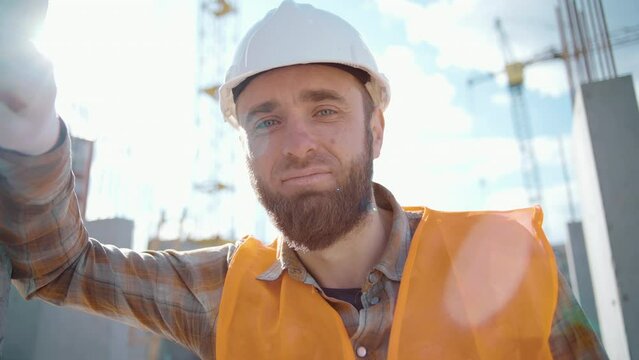 A tired worker at a construction site rests his hand on the wall after hard work and is under stress. Close-up. Worker during a break at the construction of a road on a sunny summer day