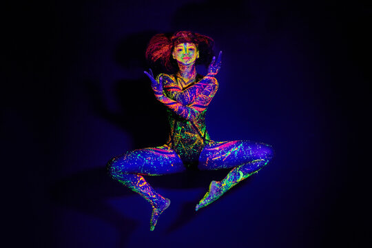 Body paint, dance and portrait of a woman in neon lighting isolated on a dark background in a studio. Creative, glow and a dancing model with psychedelic art for creativity and fluorescent abstract