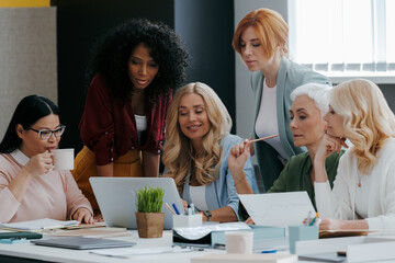 Group of confident mature women using laptop while discussing business in the office together