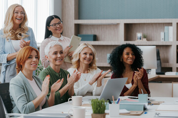 Group of mature women applauding while visiting business training class in the office