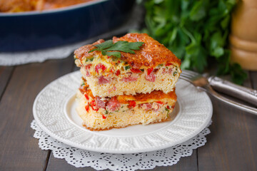 Fluffy Oven Baked omelette with cheese, tomato and ham sliced on a white ceramic plate. Vegetable Soufflé or Puffy omelet. Selective focus, horizontal, closeup, wooden table.