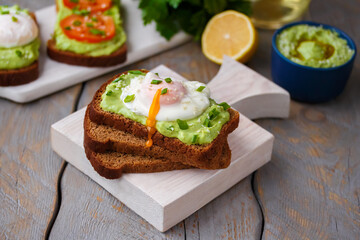 Poached Egg and Avocado Toast. Creamy avocado spread on dark bread toast with runny egg on top. Selective focus, horizontal