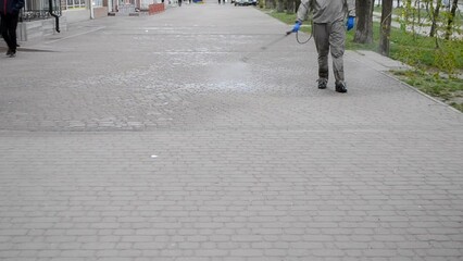 Man in protective suit spraying antiseptic solution on sidewalk in city. Persona disinfecting spray chemicals to preventing spread coronavirus. Sanitary measures in public place. Coronavirus pandemic