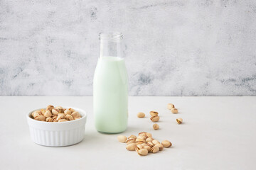 Pistachio milk in a bottle on a gray table next to pistachios. Vegetable milk. Nut milk for vegans