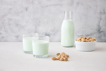 A glass of plant-based nut milk is on the table next to a bottle of pistachio milk and pistachios. The perfect drink for vegans.