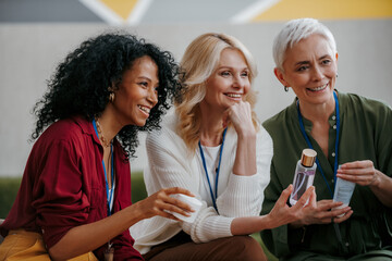 Three happy mature women examining beauty products during specialized conference