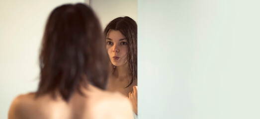 A girl in a white towel looks in the mirror and takes care of her beauty.