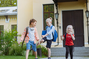 children walking from school with backpacks on sunny day. Begining of academic year. Boys by school doorstep