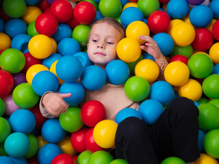 Fototapeta na wymiar Cute little girl playing on multi coloured plastic balls in big dry paddling pool in playing centre. Having fun in playroom