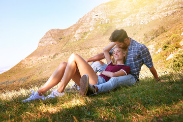 Fototapeta premium Relax, kiss and happy with couple in nature for carefree, bonding and affectionate. Happiness, date and romance with man and woman cuddle in grass field for summer break, love and mountains