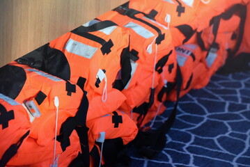 Lange Reihe mit orangen Schwimmwesten auf einem Schiff - obrazy, fototapety, plakaty