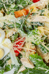 Traditional caesar salad in a white bowl on a old white table with leaves and a sauce boat and parmesan. Selected focus.