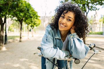 Portrait of happy young beautiful woman on bicycle smiling at camera at city park