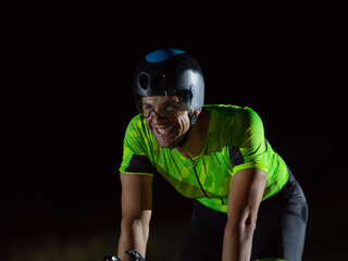 A triathlete rides his bike in the darkness of night, pushing himself to prepare for a marathon. The contrast between the darkness and the light of his bike creates a sense of drama and highlights the
