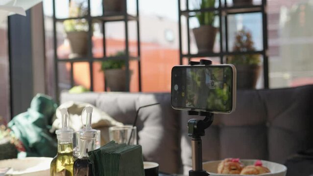 vlogger vlog blogger shooting video cafe smartphone stand tripod table camera on. cellphone device screen take video record girl female doing selfie for streaming social media lunch time meal indoors